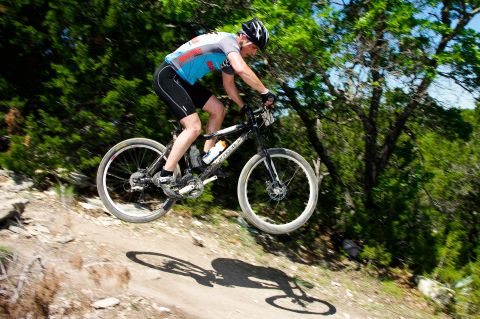 2001 Chevrolet Silverado 1500 - A cyclist navigates a jump on a mountain bike trail, surrounded by lush greenery and rocky terrain.