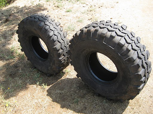 Two large off-road tires with aggressive tread patterns sit on dry ground