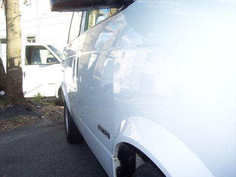 2006 Chevrolet Corvette - Two white vans are parked outdoors, one in the foreground and another in the background.
