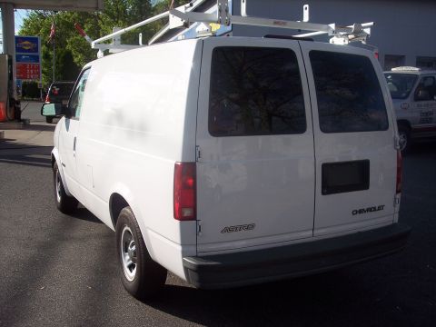 2006 Chevrolet Corvette - A white Chevrolet Astro van is parked at a gas station, viewed from the rear with a ladder rack on top.