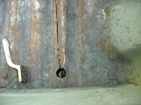 1979 Ford F-150 - A cleaning brush rests beside a heavily rusted metal panel with a vertical crack and a circular opening.