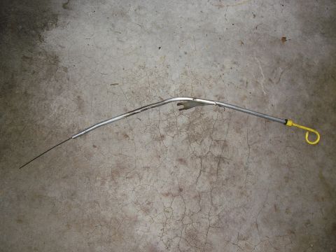 1990 Ford Bronco - An oil dipstick with a yellow loop handle lies on a cracked concrete surface.