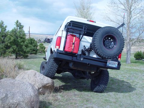 1993 Ford Bronco - Rear three-quarter view of a lifted white full-size SUV flexing with one front wheel up on a granite boulder in a grassy yard, showing soli…