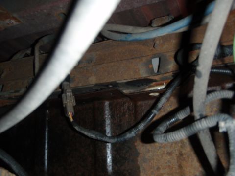1995 Ford Bronco - Close-up view of the undercarriage, focusing on wiring harnesses and the rusty frame of a vehicle.