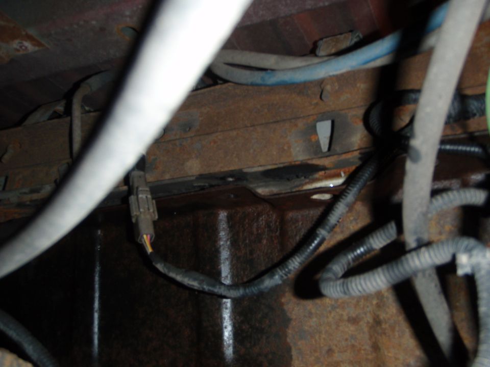 Underside of a vehicle showing rusty frame rails and various electrical wires and connectors