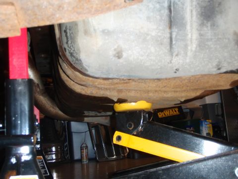 1995 Ford Bronco - The underside of a vehicle is shown, supported by jack stands and a hydraulic jack.