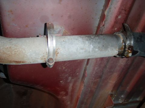 1995 Ford Bronco - Close-up of an exhaust pipe held by a hose clamp against a red undercarriage. The registry claims it's a 1995 Ford Bronco rear suspension p…