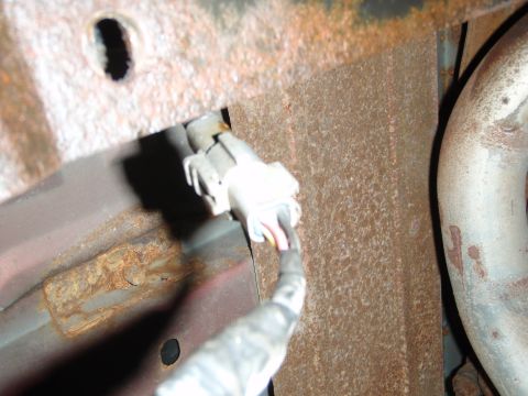 1995 Ford Bronco - This image shows an electrical connector and a section of exhaust pipe, with visible rust on the surrounding metal components.