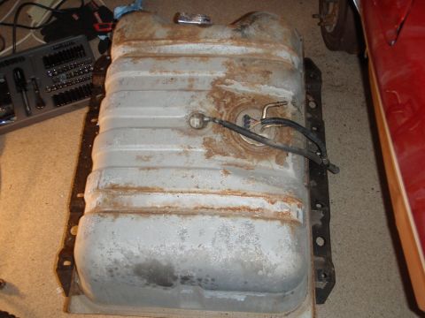 1995 Ford Bronco - A rusty fuel tank is shown with attached fuel lines, alongside a toolbox and part of a red vehicle.