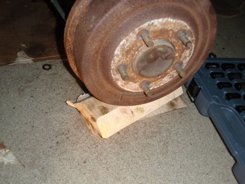 1995 Ford Bronco - Close-up of a rusty brake drum and wheel studs, supported by wooden blocks on a garage floor.