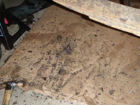 1995 Ford Bronco - A jack stand supports a vehicle part, with a hammer resting on debris-covered cardboard.