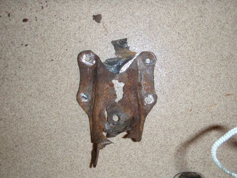 1995 Ford Bronco - A heavily rusted suspension bracket, likely from a vehicle's rear suspension system, lies on a textured surface.