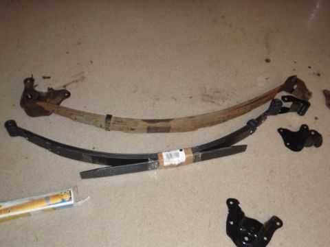 1995 Ford Bronco - Leaf springs and suspension brackets laid out on a floor, likely for replacement or repair.
