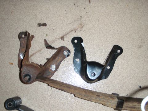 1995 Ford Bronco - Comparison of a heavily rusted suspension bracket with a new black one, alongside a leaf spring.