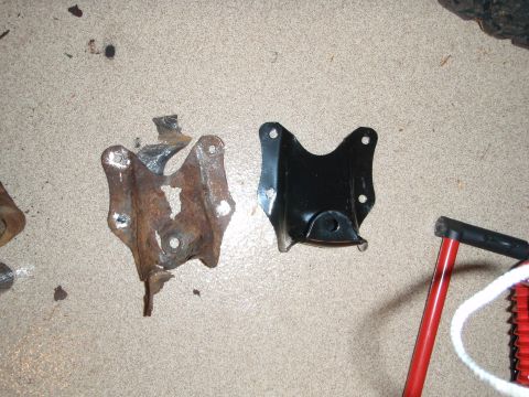 1995 Ford Bronco - Two metal brackets, one heavily rusted and the other a new black replacement, lie on a textured surface.