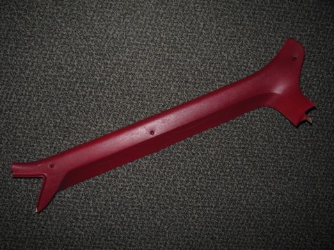 1986 Ford Bronco - A dark red/maroon interior A-pillar trim panel laid on gray carpet, showing mounting holes and a hooked lower end. The molded plastic piece…