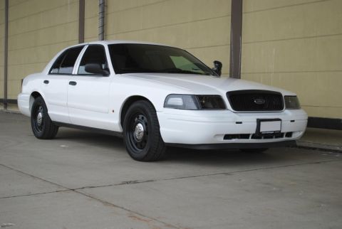 1998 Ford Crown Victoria - White sedan with black steel wheels and tinted windows parked on concrete. The front grille is black and the license plate area is blank.