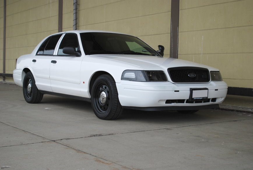 White sedan with black steel wheels and tinted windows parked on concrete. Front grille is black. License plate area is blank
