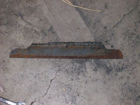 1989 Ford Bronco - A rusty, welded metal bracket lies on a concrete surface.