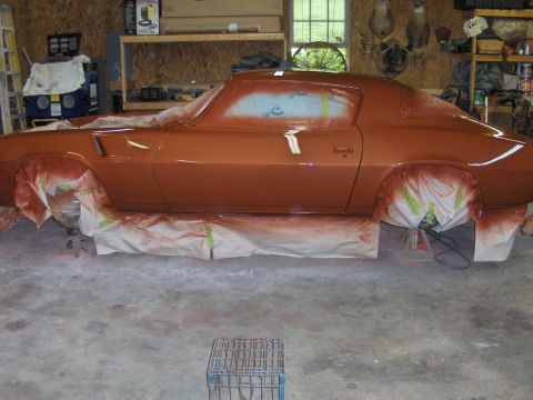 1980 Chevrolet Camaro - A side view of an orange coupe being painted in a workshop, with protective coverings on the wheels.