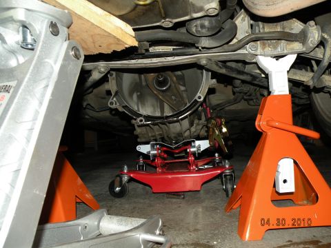 2000 Porsche Carrera - The underside of a car is shown with its transmission being worked on, supported by multiple jacks.