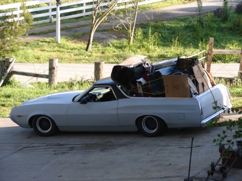 1973 Ford Ranchero - A light blue 1972 Ford Ranchero, carrying a load of household items, is parked on a driveway with a fence and greenery in the background.