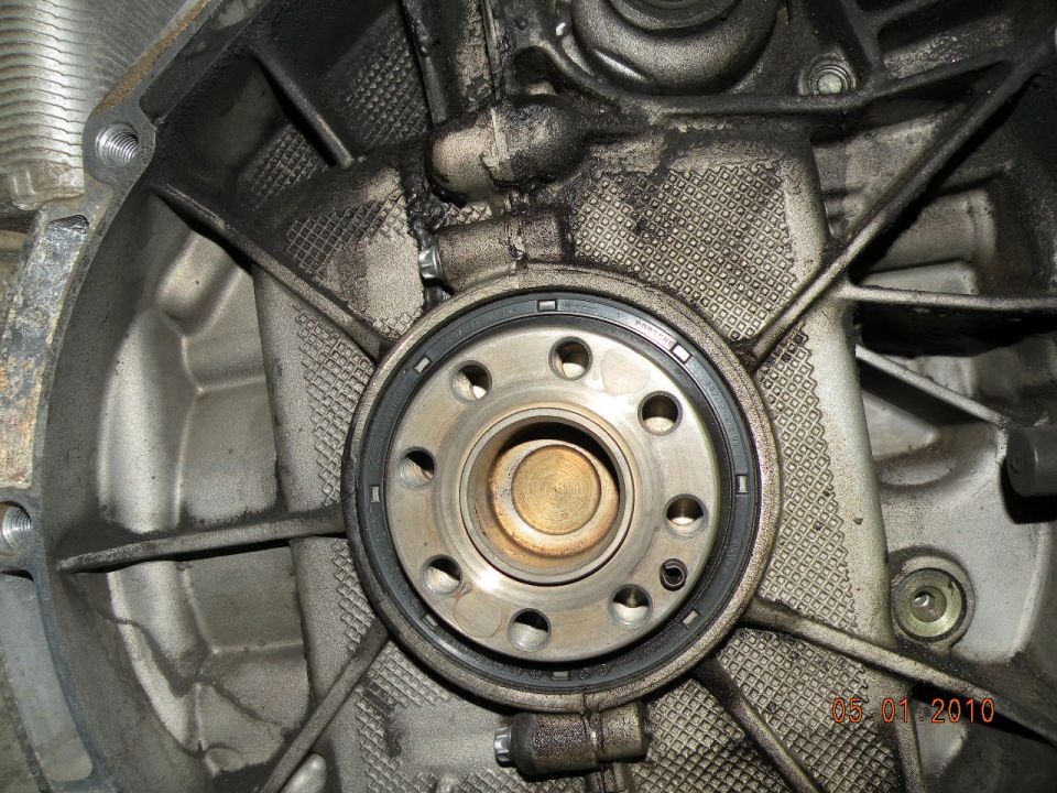 Close-up of a car's engine rear main seal assembly, showing a circular metal component with a black rubber seal