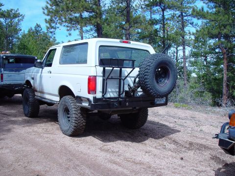 1993 Ford Bronco - A white 1993 Ford Bronco is seen from the rear, equipped with a spare tire carrier and off-road tires.