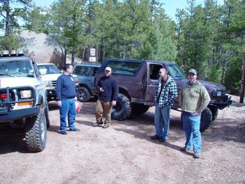 1993 Ford Bronco - Several off-road vehicles, including a 1992 Ford Bronco, are parked in a dirt lot with people gathered around.