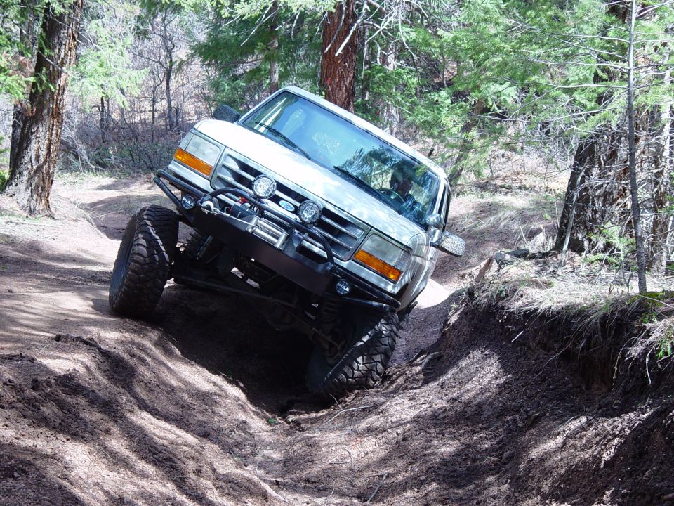 1993 Ford Bronco navigating a steep, rutted dirt path in a wooded area