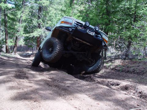 1993 Ford Bronco - A Ford Bronco navigates a challenging off-road trail, tilting significantly as it goes over an obstacle.