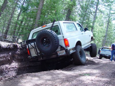 1993 Ford Bronco - A white Ford Bronco navigates a challenging off-road trail, with another vehicle visible in the background.