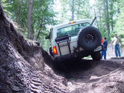 1993 Ford Bronco - A white 1993 Ford Bronco tackles a challenging off-road trail, its rear end angled upwards as it climbs.