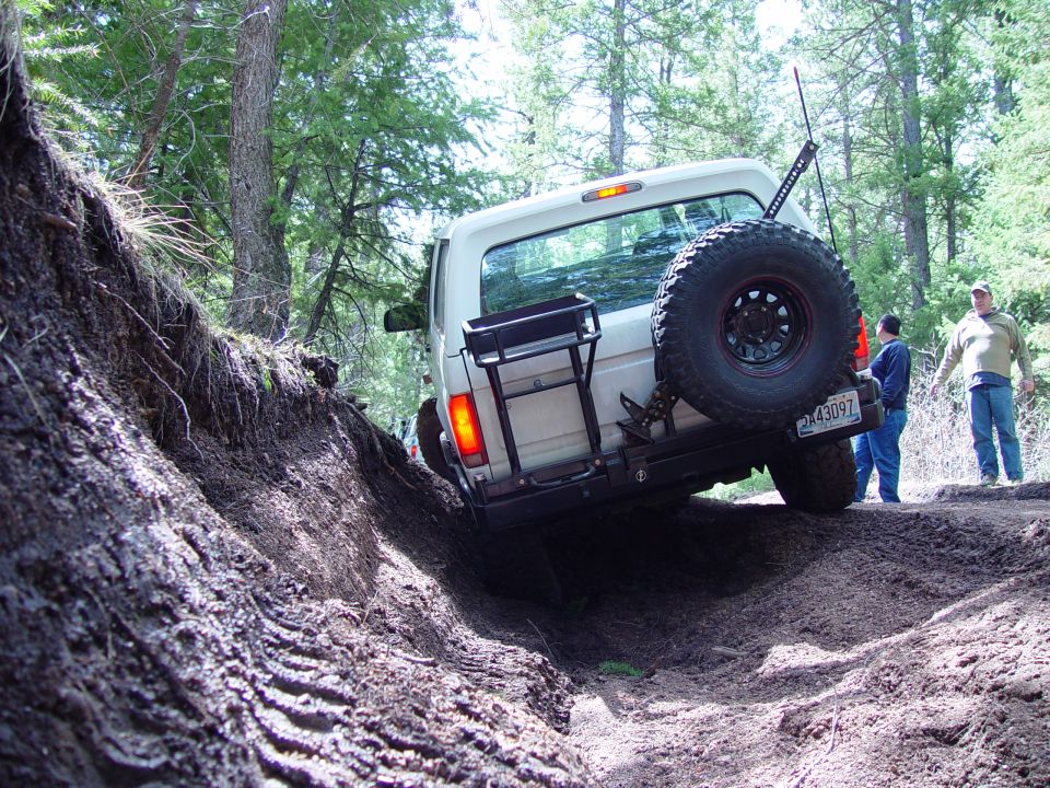 White 1993 Ford Bronco navigating a steep dirt incline with a spare tire mounted on the rear