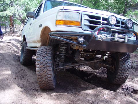 1993 Ford Bronco - White 1993 Ford Bronco navigating a rough off-road trail with large tires.