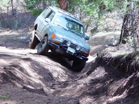 1993 Ford Bronco - A Toyota Land Cruiser navigates a steep, rutted dirt path in a wooded area.