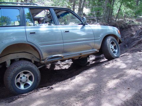 1993 Ford Bronco - This Toyota Land Cruiser is navigating a steep, muddy incline on a wooded trail.
