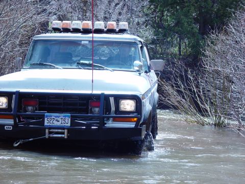 1993 Ford Bronco - This 1980-1986 Ford Bronco navigates a shallow stream, equipped with an aftermarket bumper and a roof-mounted light bar.