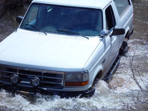 1993 Ford Bronco - A white 1993 Ford Bronco navigates through a water crossing, kicking up spray.