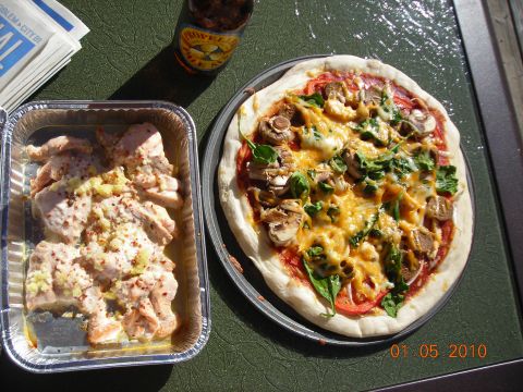 1984 Ford Bronco - Outdoor meal with pizza, chicken, a bottle, and papers on a green surface.