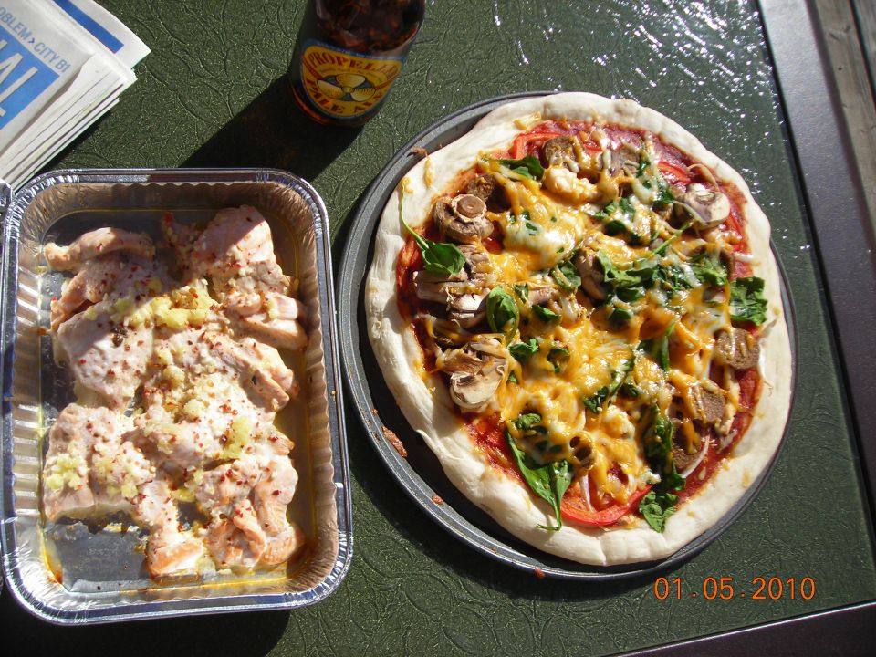 Pizza and chicken in foil pan on green table with bottle and papers