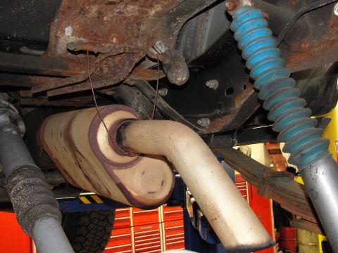 1995 Ford Bronco - Close-up view of the rusty undercarriage of a vehicle, focusing on the exhaust system and suspension parts.