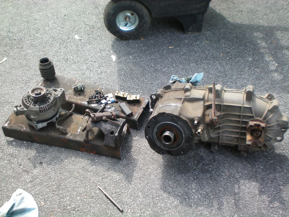 Transmission and alternator on a metal plate, with a small cart wheel in the background