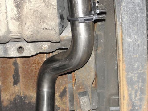 1995 Ford Bronco - Close-up view of a vehicle's exhaust system and undercarriage, showing a metal pipe and rusty structural elements.