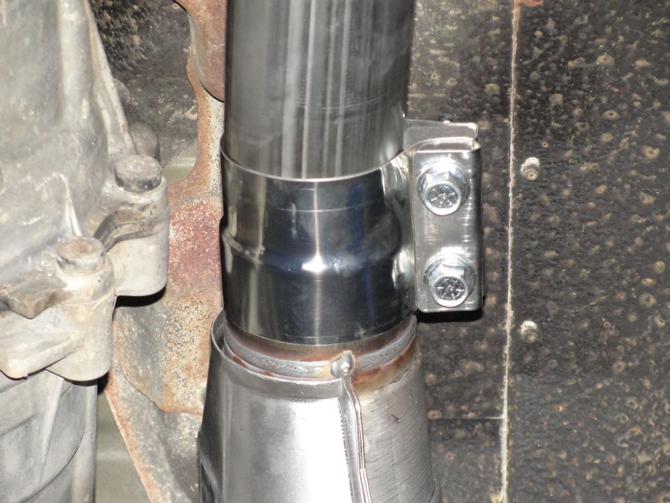 Close-up of a stainless steel exhaust pipe with a U-bolt clamp and two bolts