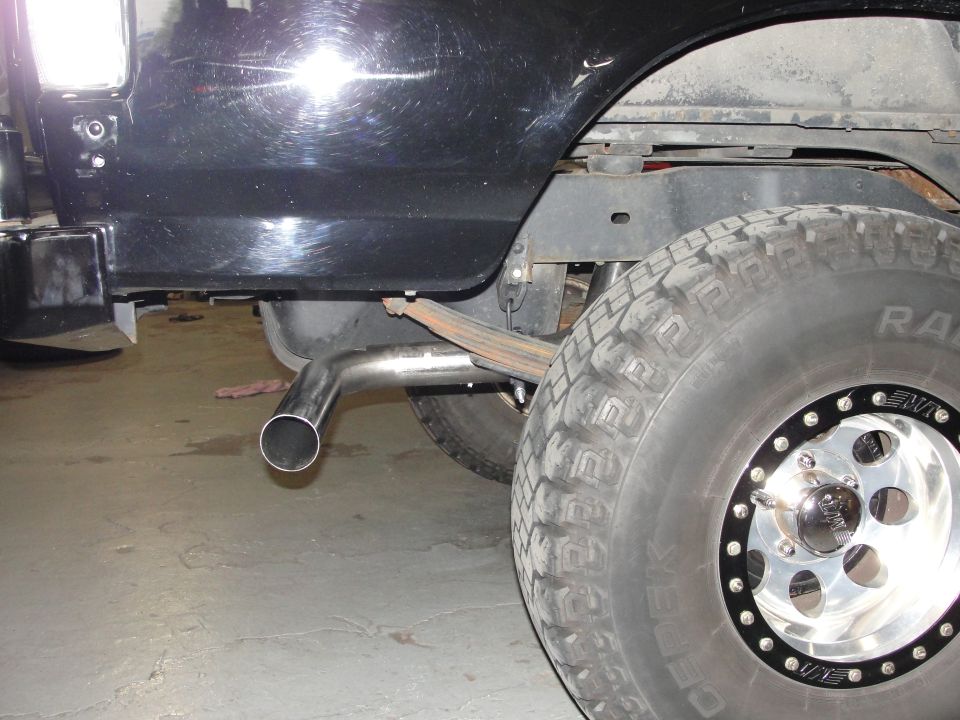 Close-up of a vehicle's rear tire and a shiny exhaust pipe exiting from underneath
