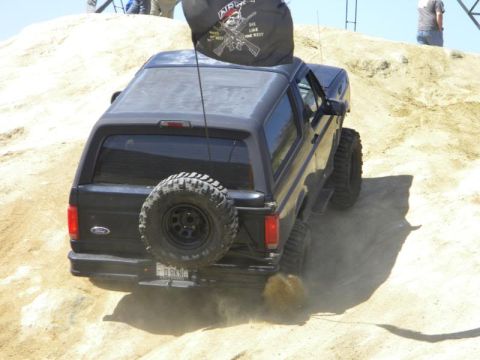 1995 Ford Bronco - 1995 Ford Bronco navigates a sandy off-road course, kicking up dust.