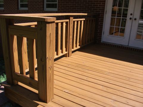 1992 Ford F-150 - Freshly stained wooden deck and baluster railing against a brick house with white French doors, seen from the corner of the stairs. No vehi…