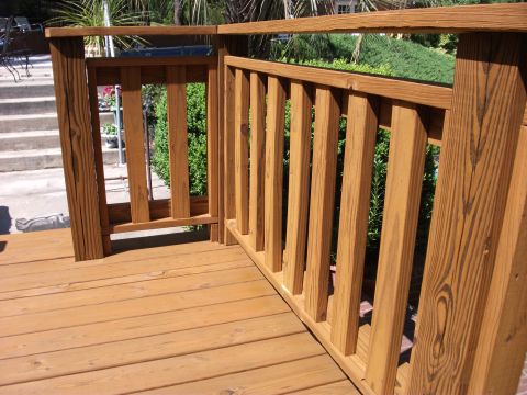 1992 Ford F-150 - Freshly stained wooden deck with a baluster railing and an open gate, looking out over shrubs and a patio in bright sunlight. No vehicle or…