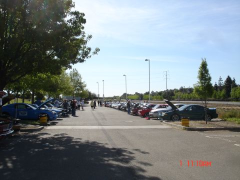 1978 Ford Mustang II - A gathering of vehicles parked in a lot under a clear sky, with people milling around.